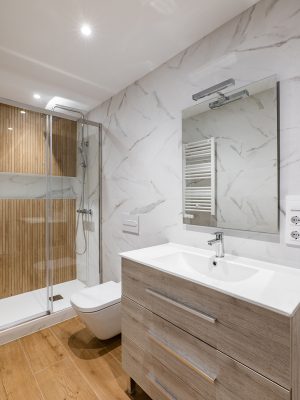 Simple and modern bathroom with marble white tiles, wooden finishing, toilet and shower.